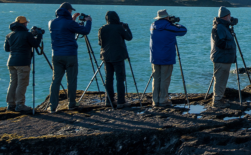 Photographers stand with their cameras on the edge of a lake